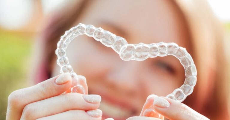 adult holds up aligners in a heart shape and wonders should I see an orthodontist or dentist for invisalign