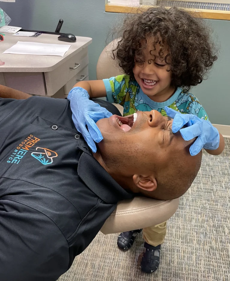 Dr. Battle in the exam chair with a young boy playfully checking his teeth